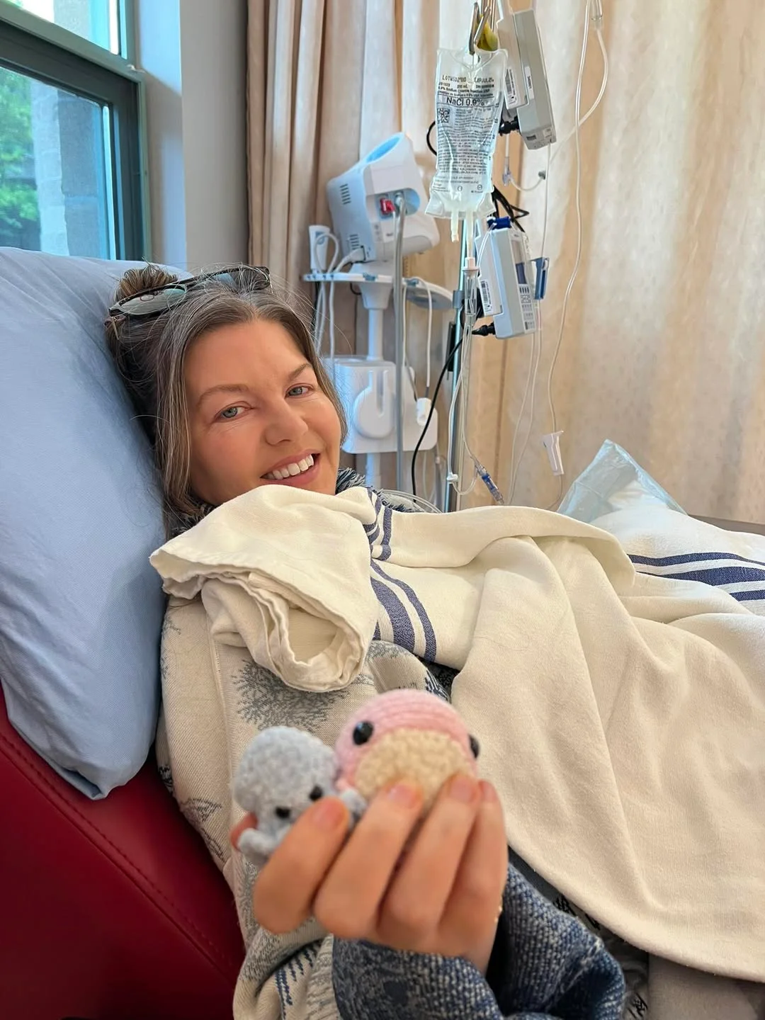 Carly holding two hand-knit stuffed animals in her hospital bed